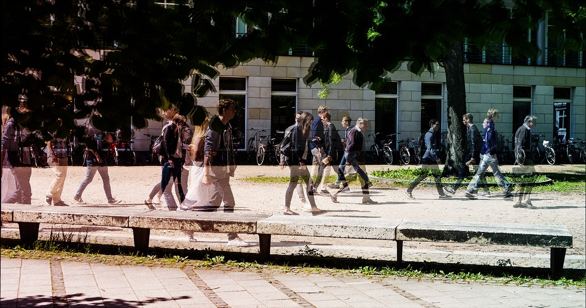 Das Bild zeigt durchschaubare Menschen vor dem Universitätsgebäude