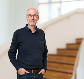 Dirk Sauerland steht vor einer Treppe, Hände in den Taschen